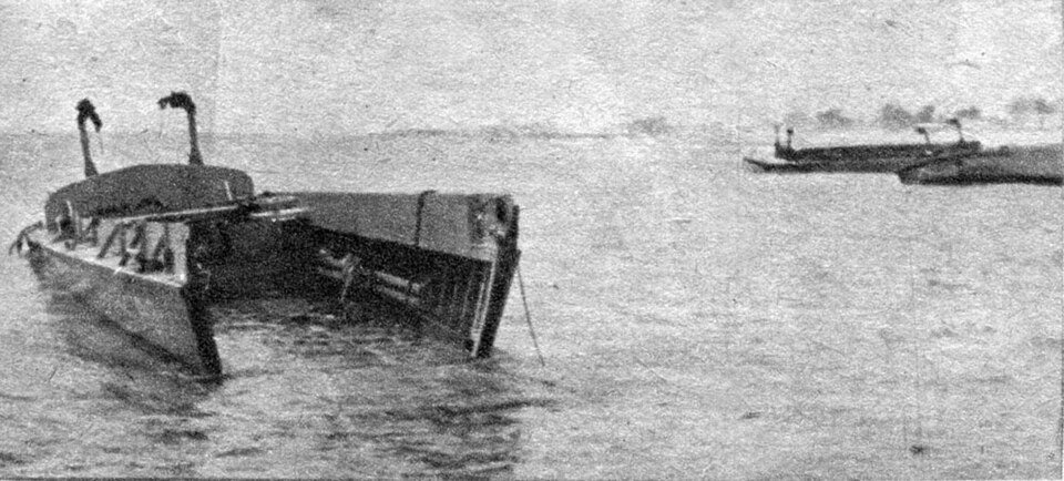 A grainy photo of an empty landing craft sitting in shallow water, with other boats in the distance.