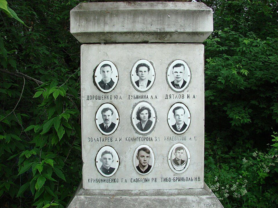 Stone grave memorial in Yekaterinburg set with nine small portrait photos of the Dyatlov group, their names carved beneath.
