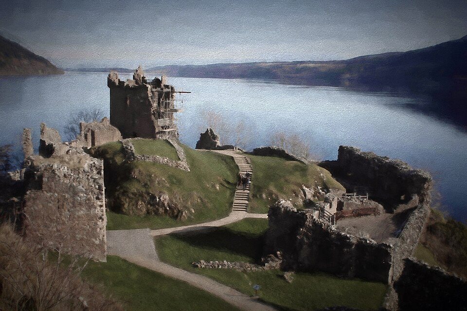 The ruins of Urquhart Castle on a green headland, with the long, dark water of Loch Ness stretching away between hills.
