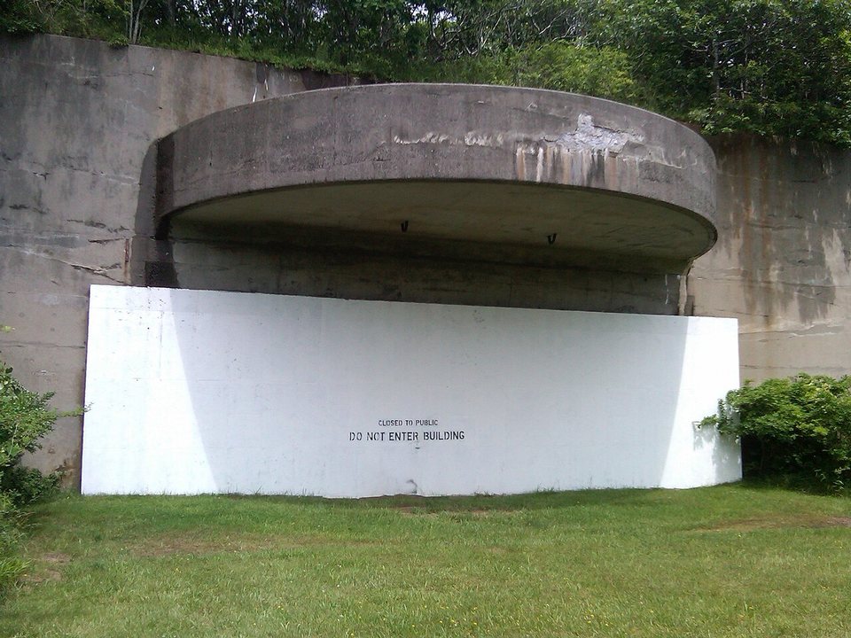 A concrete gun bunker set into a grassy hillside at Camp Hero, its opening sealed by a white panel marked Do Not Enter Building.
