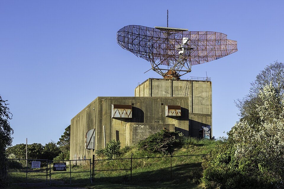 The AN/FPS-35 radar at Camp Hero: a wide lattice antenna on top of a concrete tower, behind a chain-link fence.