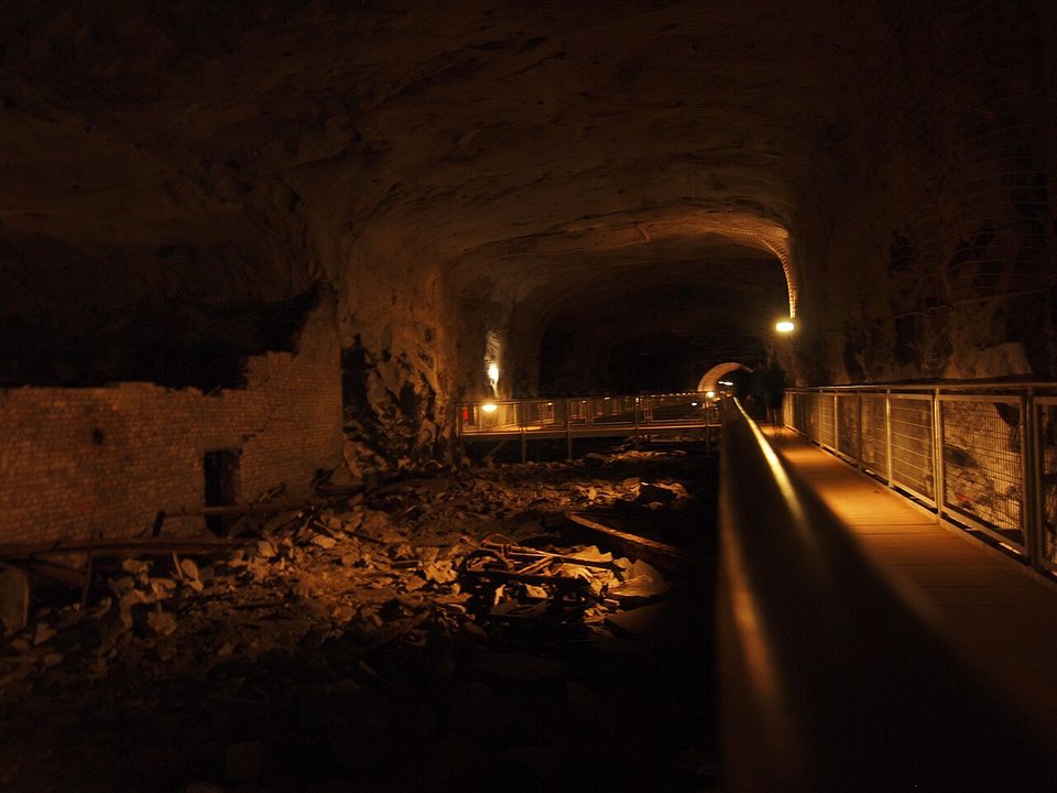A long, dim tunnel carved into rock at the Mittelbau-Dora memorial site, with a visitor walkway.