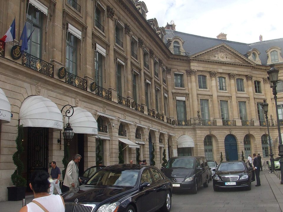 The front of the Hôtel Ritz on Place Vendôme in Paris, with white awnings over the doors and black cars parked outside.