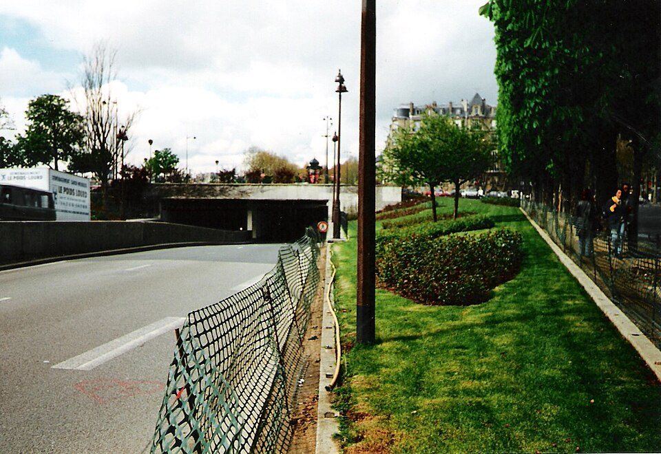 A Paris road running toward the entrance of the Alma underpass, beside a grassy median with trees.