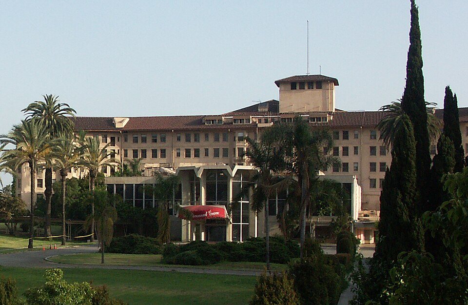 The front of the Ambassador Hotel in Los Angeles, a large pale building with palm trees, in 2004.