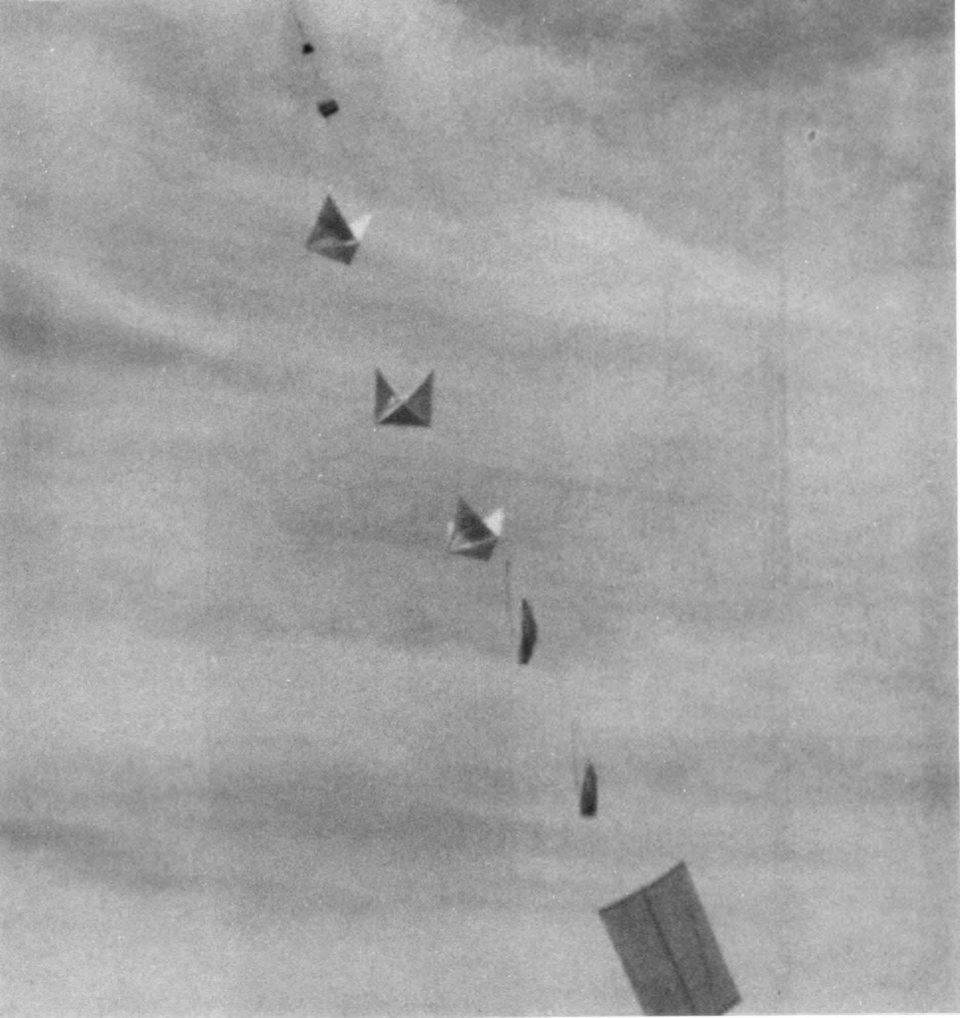 A black-and-white photo of part of a Project Mogul balloon train in flight: a line of kite-like radar reflectors and instruments hanging against a gray sky.